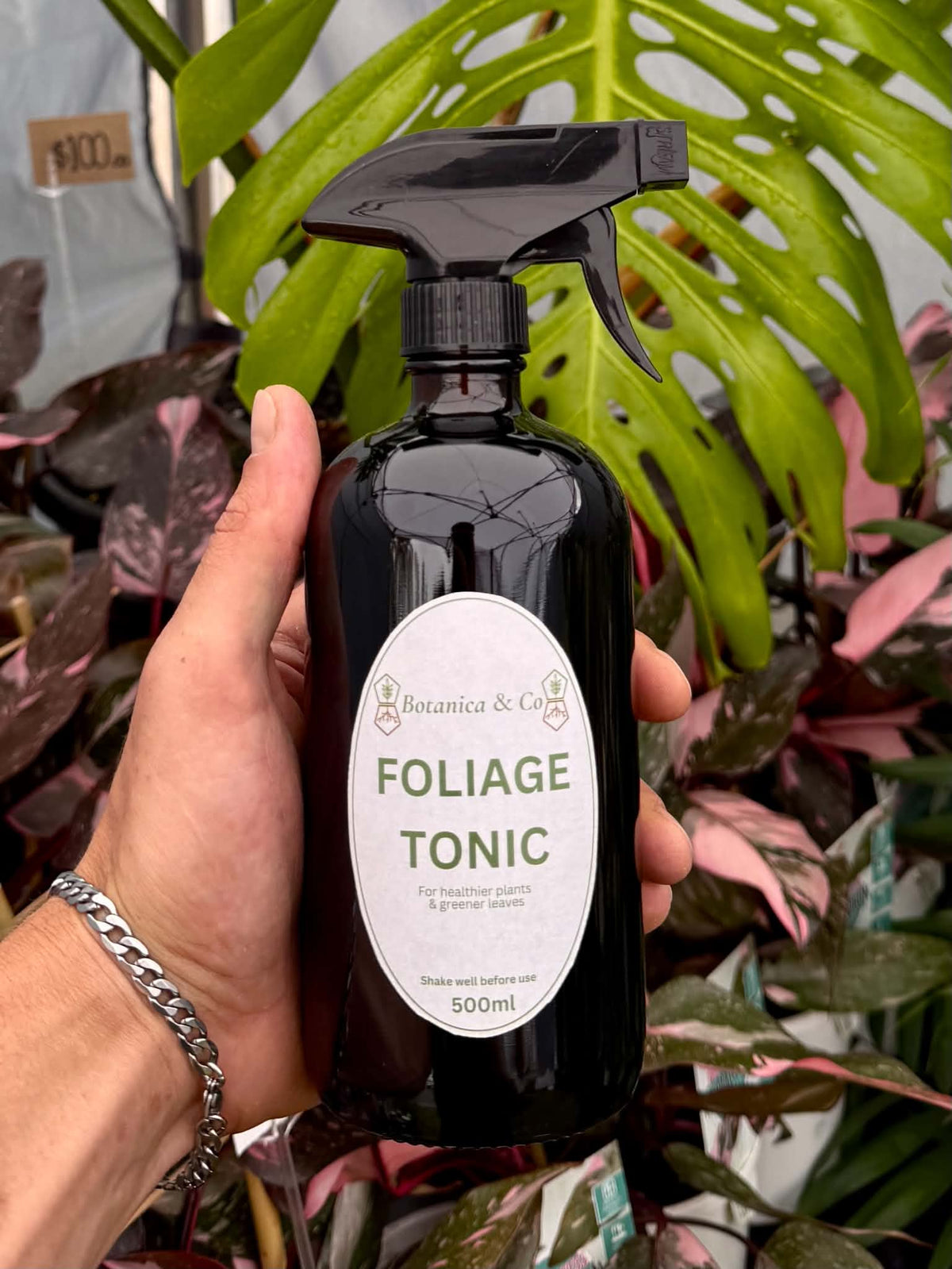 Black 500 ml Botanica & Co Foliage Tonic spray bottle held in front of foliage