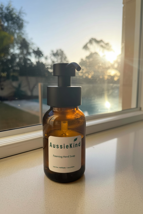 AussieKind amber glass foaming hand soap dispenser on a window sill with golden hour backlight
